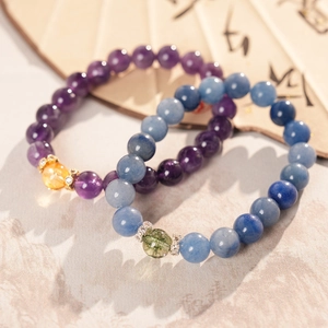 Macro detail of amethyst beaded bracelets with gold crown charms on Zen fan background