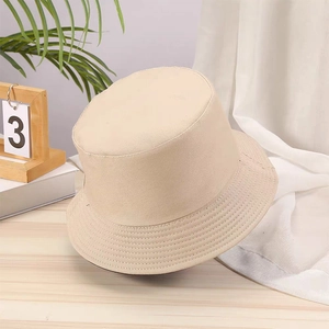 Detail of a beige cotton twill bucket hat placed on a wooden table with green plants