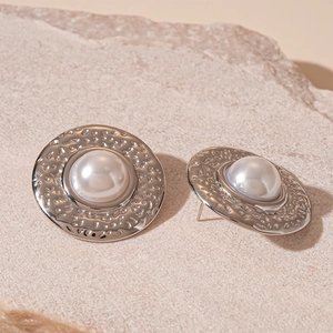 Detail of silver textured metal stud earrings with a white faux pearl center on stone