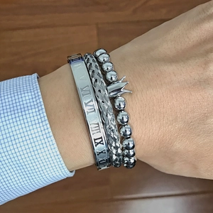 Close-up of three-piece silver men's bracelet set with Roman numerals and crown charm