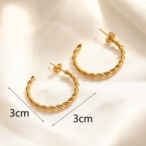 Detail view of 3cm golden twisted rope hoop earrings on soft white silk fabric background