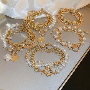 Detail of layered gold alloy chains with artificial pearls and coin charms on satin