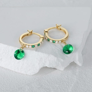 Macro shot of gold silver earrings with sparkling emerald green faceted gemstones