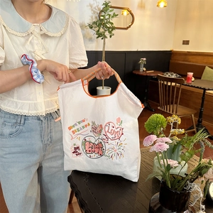 Detailansicht der weißen Canvas-Tasche mit bunter Stickerei und orangefarbenen Nähten