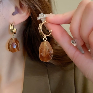 Close-up of golden C-shaped resin earrings with amber geometric pendant on model