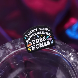 Cartoon enamel pin with I CAN'T STOP DOWNLOADING FREE FONTS text on black alloy base