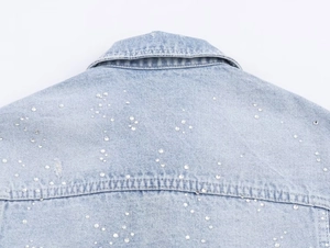 Vue détaillée d'une veste en jean bleu clair avec ornements en strass et perles