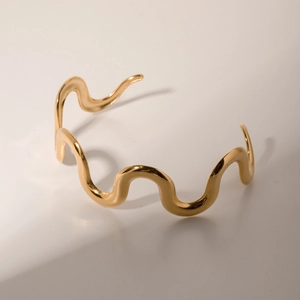 Detailed close-up of a 18k gold plated stainless steel wavy bangle on a white background