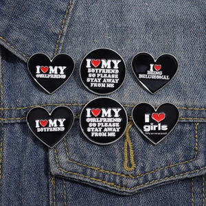 Set of 6 black enamel heart brooches with white text pinned on denim jacket pocket