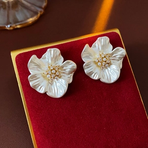 Macro shot of white flower earrings with mother-of-pearl luster on red velvet padding