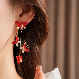 Détail de boucles d'oreilles pendantes papillon rouge avec dorure et zircons