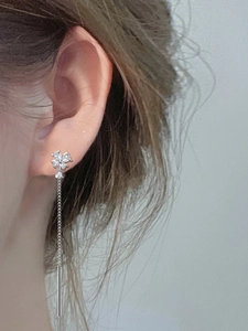 Close-up detail of silver long chain tassel earrings with flower stud on a model