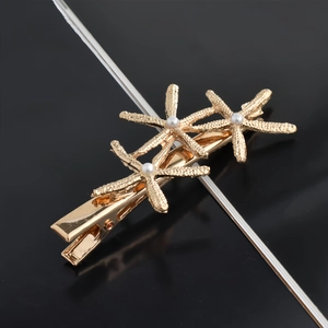 Detailed view of golden starfish hair clips with elegant pearls on a black surface