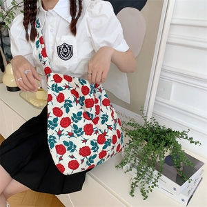 Detail of red rose floral print on a white canvas shoulder bag worn by a model