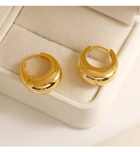 Close-up of minimalist 18K gold chunky hoop earrings on a cream leather jewelry box