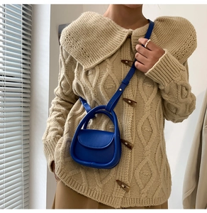 Détail du mini sac en cuir bleu roi avec poignée demi-ronde sur un pull en maille beige