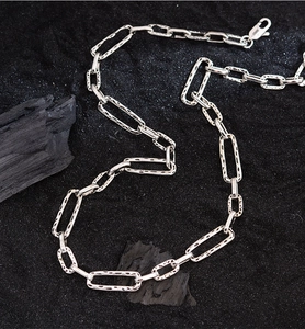 Close-up of silver paperclip chain necklace with hammered texture on black background