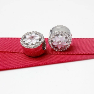 Silver bead with pink magnolia flower pattern and rhinestones on a red ribbon