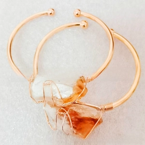 Detail of rose gold wire-wrapped open cuff bracelets with irregular natural raw stones
