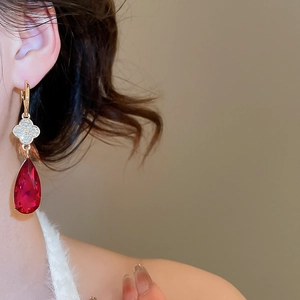 Close-up of golden drop earring with diamond clover and red pear-shaped crystal