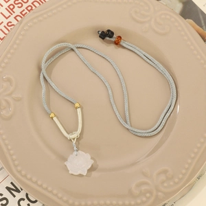 Macro detail of enamel calla lily pendant with white pearl on a light blue woven cord