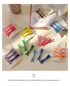 Macro shot of matte colorful X-shaped hair clips arranged on white textured cardstock