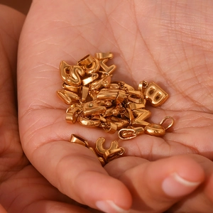 Macro view of tiny 18K gold plated bubble initial pendants displayed in a palm