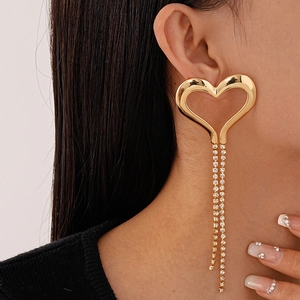 Close-up of golden hollow heart earrings with shimmering rhinestone tassels on a model