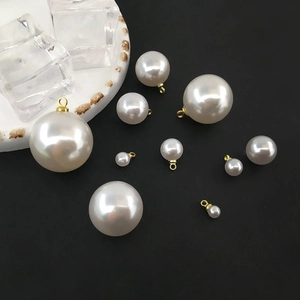Various sizes of cream imitation pearl pendants with gold loops on a black background