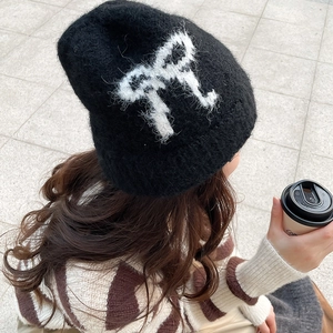 Top view of a black mohair knit beanie featuring a white bow design worn outdoors