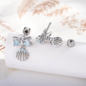 Micro-inlaid zircon bow shell stud earrings in silver with blue stones on plant background