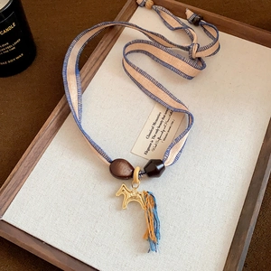 Detail of 24k gold-plated pony pendant with blue silk tassels and woven ribbon necklace