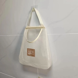 Close-up of wall-mounted mesh storage bag with leather patch and hanging rope on gray tiles