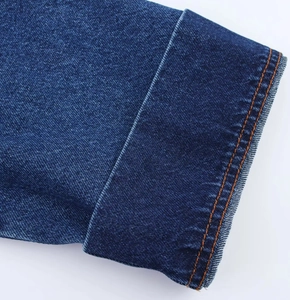 Dettaglio del polsino della giacca di jeans blu scuro con cuciture arancioni a contrasto