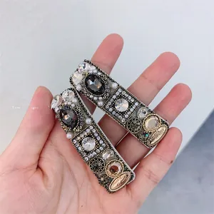 Macro view of vintage style BB clips with grey rhinestones, pearls and woven gold texture