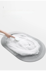 Detail of cleaning a grey oval anti-slip bath mat with a brush and rich soap foam