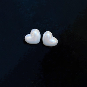 Close-up of pearl heart stud earrings featuring soft iridescent luster on dark background