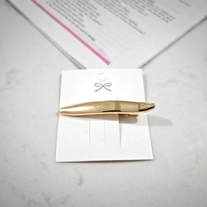 Macro detail of golden metal hair clip with brushed texture on elegant marble background