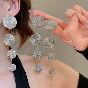 Close-up of textured round metal discs on long silver tassel earrings worn by a model