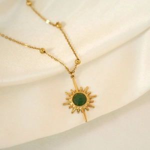 Detailed shot of 14K gold-plated starburst pendant with green stone on satin fabric
