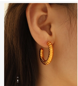 Macro shot of gold hollow C-shaped hoop earrings with textured spiral design worn by model