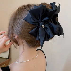 Detail of a large black satin bow hair claw with a rhinestone center on a stylish updo