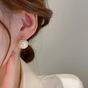 Close-up of a minimalist gold-plated pearl hoop earring worn by a model on her ear