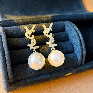 Détail de boucles d'oreilles dorées avec logo en zircon et perle blanche sur velours