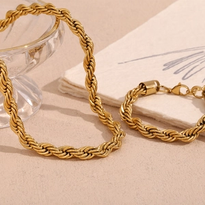 Detail of 18K gold plated rope chain necklace and bracelet set on a decorative surface