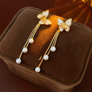 Primer plano de pendientes de mariposa dorados con borlas de perlas en un estuche