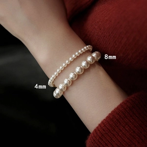 Detailed view of 4mm and 8mm pearl elastic bracelets worn on a wrist against a red background