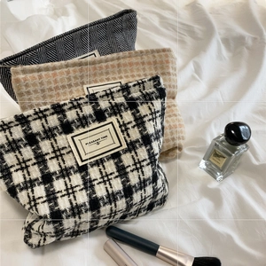 Large plaid tweed cosmetic bag with zipper and decorative patch on a fabric background