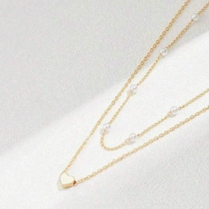 Double-layered gold necklace featuring white pearls and a minimalist heart pendant