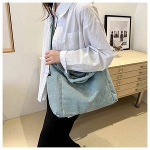 Detail of light blue corduroy tote bag worn by a model in a minimalist home setting